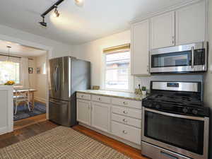 Kitchen featuring light stone countertops, white cabinetry, dark hardwood / wood-style floors, decorative light fixtures, and appliances with stainless steel finishes