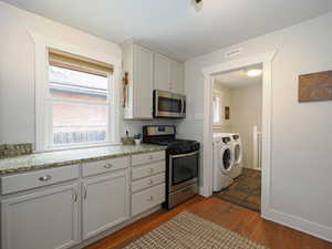 Kitchen with light stone countertops, dark hardwood / wood-style flooring, washer and dryer, and appliances with stainless steel finishes