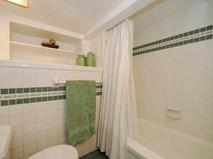 Bathroom featuring shower / bathtub combination with curtain, tile walls, and toilet