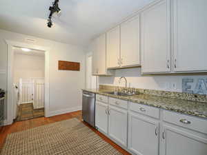 Kitchen with dark hardwood / wood-style flooring, track lighting, stainless steel dishwasher, sink, and white cabinetry