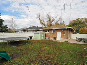 Rear view of house featuring a patio, central AC unit, a yard, a trampoline, and a storage unit