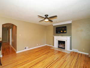 Unfurnished living room with a tile fireplace, a textured ceiling, light hardwood / wood-style flooring, and ceiling fan