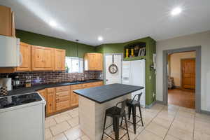 Kitchen featuring a center island, light brown cabinets, a kitchen breakfast bar, pendant lighting, and white appliances