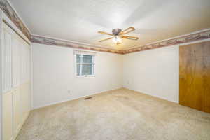 Unfurnished bedroom featuring a textured ceiling, ceiling fan, and light carpet