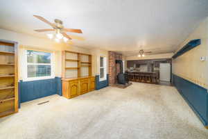 Living room with carpet, a textured ceiling, a wood stove, and ceiling fan