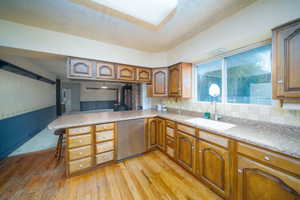 Kitchen featuring sink, stainless steel dishwasher, kitchen peninsula, light hardwood / wood-style floors, and a kitchen bar