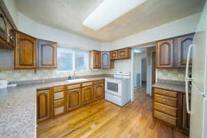 Kitchen with sink, stove, light hardwood / wood-style floors, a textured ceiling, and decorative backsplash