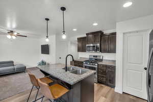 Kitchen featuring light stone countertops, appliances with stainless steel finishes, decorative light fixtures, light hardwood / wood-style flooring, and a center island with sink