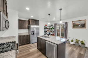 Kitchen featuring light stone countertops, sink, light hardwood / wood-style floors, pendant lighting, and appliances with stainless steel finishes