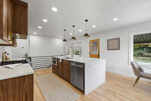 Kitchen featuring pendant lighting, a center island with sink, sink, light hardwood / wood-style flooring, and stainless steel appliances