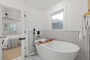 Bathroom featuring ceiling fan, a bathtub, and tile walls