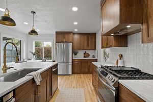 Kitchen with sink, light hardwood / wood-style flooring, premium range hood, pendant lighting, and appliances with stainless steel finishes