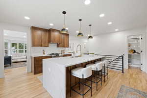 Kitchen with backsplash, stainless steel gas range, decorative light fixtures, light hardwood / wood-style flooring, and a large island