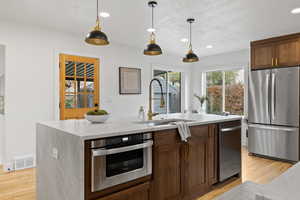 Kitchen featuring sink, an island with sink, stainless steel appliances, and light wood-type flooring