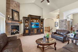 Living room with a stone fireplace, ceiling fan, carpet floors, and high vaulted ceiling