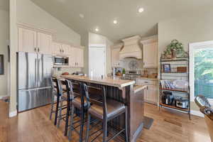 Kitchen featuring custom exhaust hood, light hardwood / wood-style flooring, appliances with stainless steel finishes, and vaulted ceiling