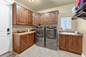 Laundry area featuring separate washer and dryer, sink, light tile patterned floors, and cabinets