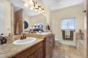 Bathroom with tile patterned flooring, vanity, a relaxing tiled tub, and toilet