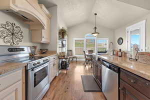 Kitchen with dark brown cabinetry, stainless steel appliances, light hardwood / wood-style flooring, vaulted ceiling, and custom exhaust hood