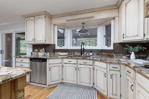 Kitchen featuring sink, hanging light fixtures, stainless steel dishwasher, light stone countertops, and light wood-type flooring