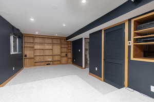 Basement featuring built in shelves and light colored carpet