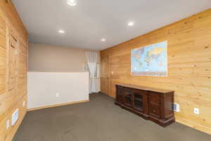 Unfurnished living room featuring wooden walls and dark colored carpet