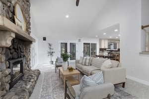 Carpeted living room featuring a stone fireplace, sink, and high vaulted ceiling