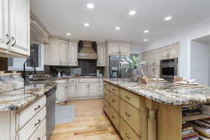 Kitchen with a center island, premium range hood, sink, light stone countertops, and appliances with stainless steel finishes