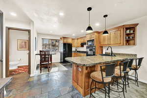 Kitchen featuring black appliances, sink, hanging light fixtures, a kitchen bar, and kitchen peninsula