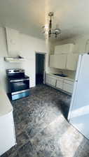 Kitchen with ventilation hood, pendant lighting, white cabinets, white fridge, and stainless steel range with electric cooktop