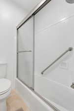 Bathroom featuring tile patterned flooring, toilet, and bath / shower combo with glass door