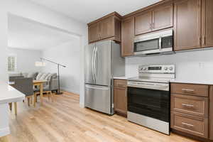 Kitchen with dark brown cabinetry, stainless steel appliances, and light hardwood / wood-style flooring