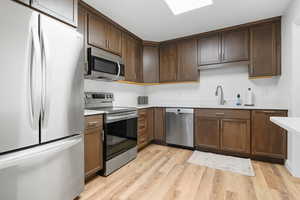 Kitchen featuring sink, light hardwood / wood-style flooring, dark brown cabinets, and appliances with stainless steel finishes