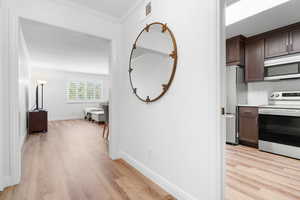 Hallway with light hardwood / wood-style flooring and crown molding