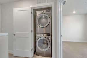 Laundry area featuring light carpet and stacked washer and clothes dryer