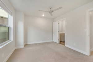 Unfurnished bedroom with connected bathroom, ceiling fan, and light colored carpet