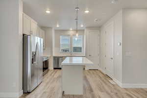 Kitchen featuring appliances with stainless steel finishes, pendant lighting, white cabinetry, light hardwood / wood-style floors, and a kitchen island