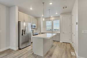 Kitchen featuring a center island, sink, light hardwood / wood-style flooring, decorative light fixtures, and stainless steel appliances