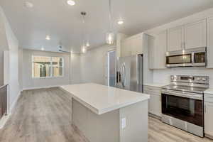 Kitchen with pendant lighting, a center island, decorative backsplash, light wood-type flooring, and stainless steel appliances