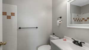 Bathroom featuring tiled shower, vanity, and toilet