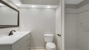 Bathroom featuring a tile shower, vanity, and toilet