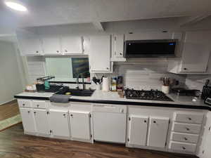 Kitchen with backsplash, sink, dark hardwood / wood-style floors, appliances with stainless steel finishes, and white cabinetry