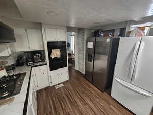 Kitchen featuring dark hardwood / wood-style flooring, a textured ceiling, exhaust hood, black appliances, and white cabinets