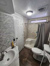 Bathroom with backsplash, toilet, walk in shower, a textured ceiling, and wood-type flooring