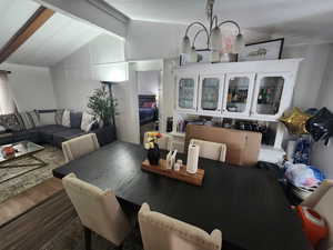 Dining area with dark wood-type flooring, lofted ceiling with beams, and an inviting chandelier