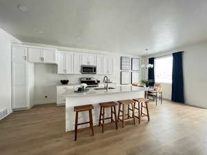 Kitchen featuring sink, appliances with stainless steel finishes, a kitchen island with sink, white cabinets, and light wood-type flooring