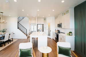 Kitchen with white cabinetry, hanging light fixtures, an island with sink, wood-type flooring, and appliances with stainless steel finishes