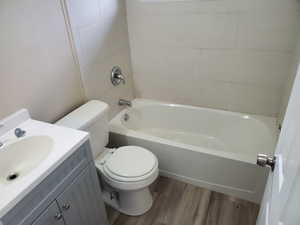 Full bathroom featuring hardwood / wood-style floors, tiled shower / bath combo, toilet, and vanity