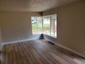 Empty room with a textured ceiling and dark wood-type flooring