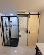 Washroom featuring a barn door and stacked washer / dryer